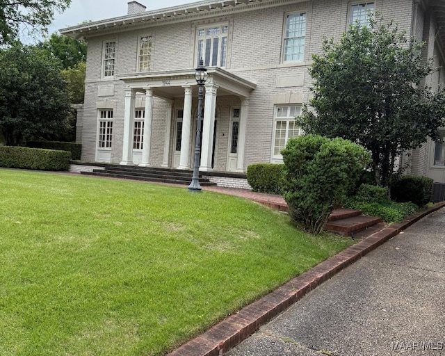 view of front facade featuring a front lawn, central air condition unit, a chimney, and brick siding