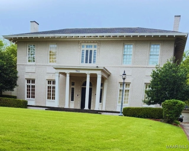 view of front of property with a chimney, brick siding, and a front lawn