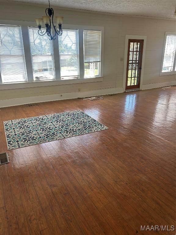unfurnished dining area featuring wood-type flooring, visible vents, baseboards, and a notable chandelier