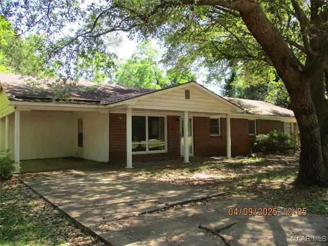 back of property featuring driveway, a carport, and brick siding