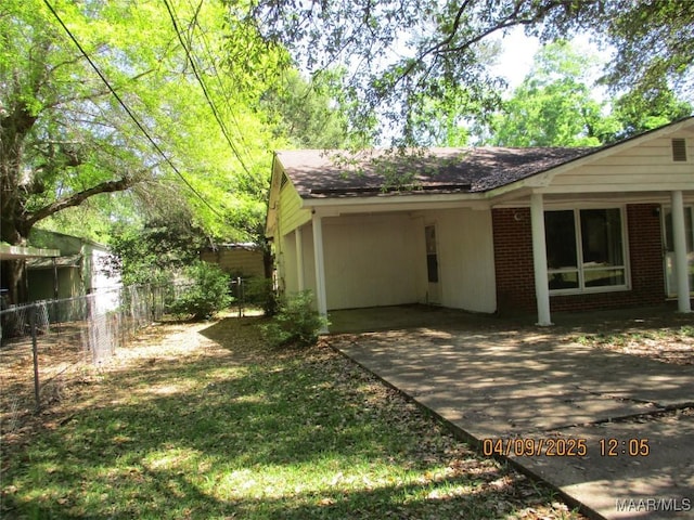 view of property exterior with brick siding, fence, driveway, and an attached carport