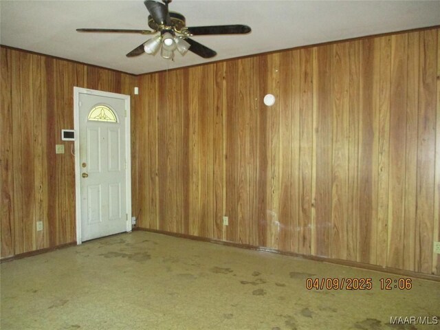 entryway with a ceiling fan, wood walls, carpet floors, and baseboards