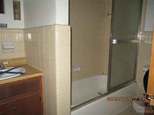 bathroom with bath / shower combo with glass door, toilet, vanity, and tile walls