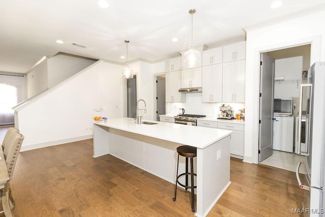 kitchen featuring a sink, under cabinet range hood, recessed lighting, a center island with sink, and refrigerator with ice dispenser