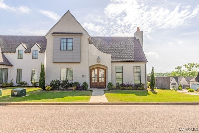 view of front of home with a chimney, brick siding, french doors, and a front lawn