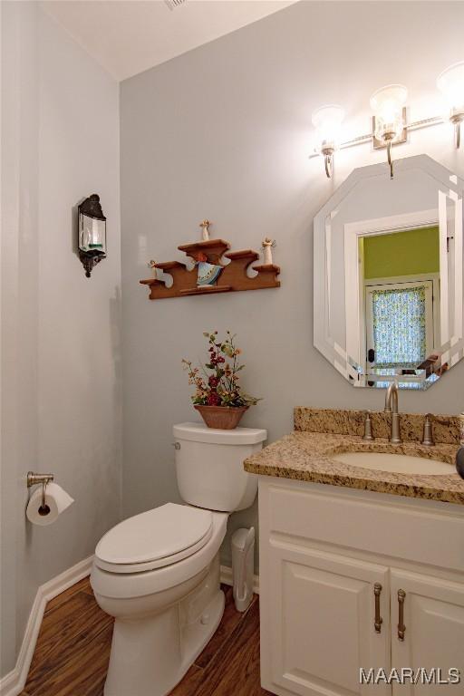 bathroom with toilet, vanity, wood finished floors, and baseboards