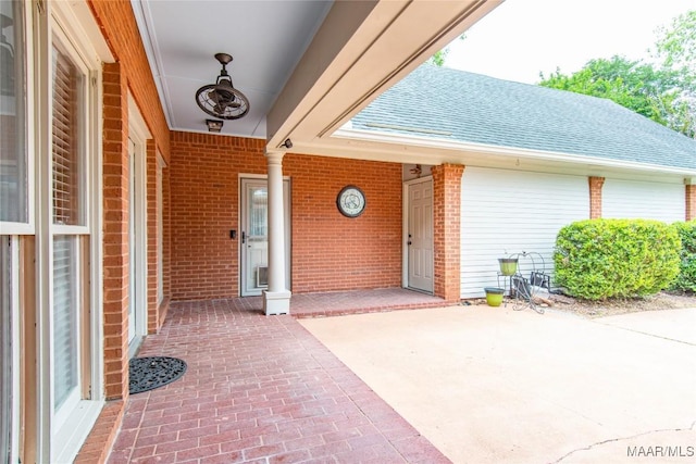 property entrance with a patio, a shingled roof, and brick siding