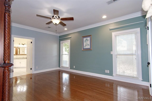 spare room with crown molding, visible vents, ceiling fan, baseboards, and wood finished floors