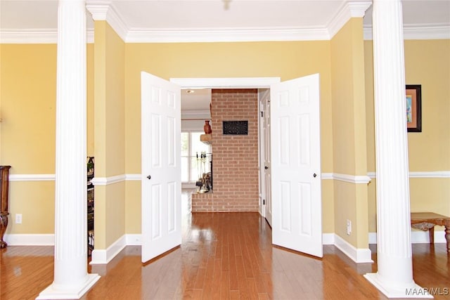 hall with ornamental molding, decorative columns, wood finished floors, and baseboards