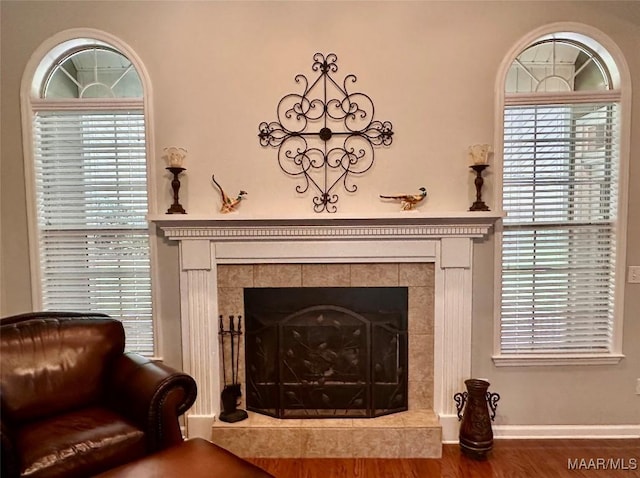 interior details featuring wood finished floors, a tiled fireplace, and baseboards