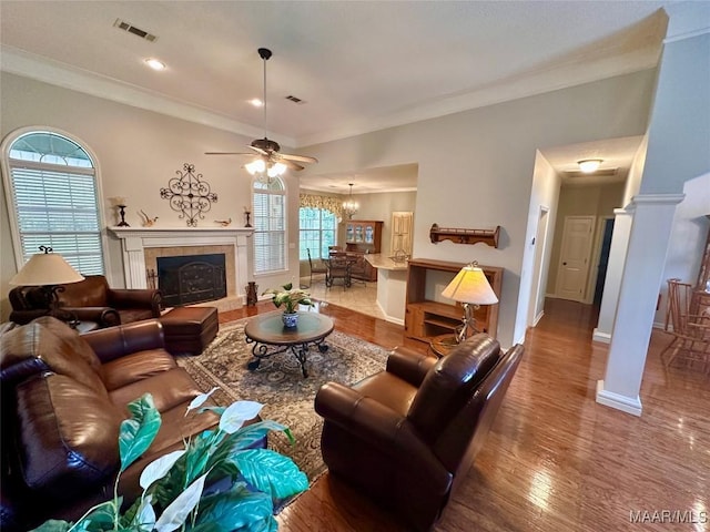 living room featuring a fireplace, visible vents, baseboards, ornamental molding, and wood finished floors