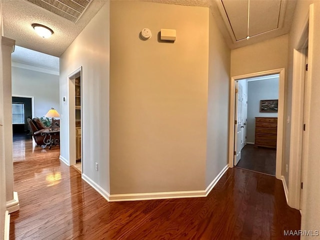 corridor featuring a textured ceiling, visible vents, baseboards, attic access, and wood finished floors