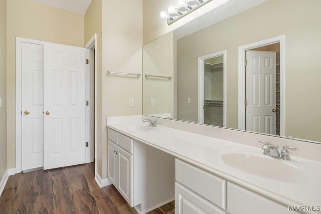 full bathroom with baseboards, wood finished floors, double vanity, and a sink