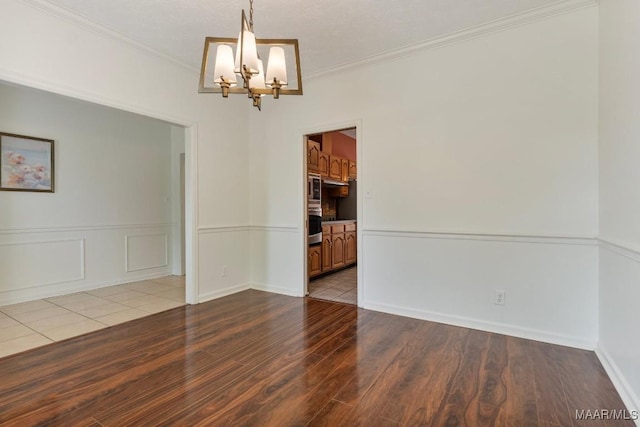spare room featuring an inviting chandelier, wood finished floors, and crown molding