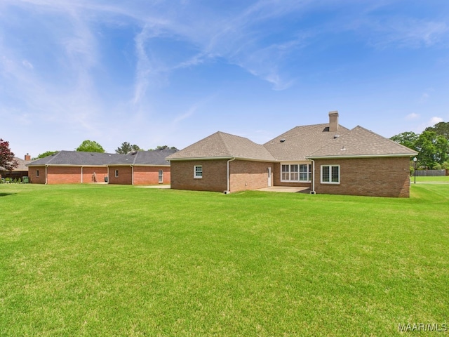 back of property featuring a lawn, a chimney, a patio area, and brick siding