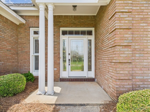 view of exterior entry featuring brick siding and a porch