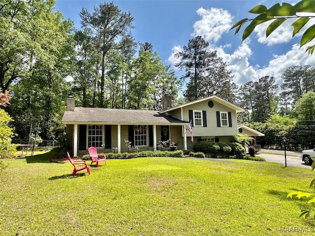 split level home featuring a chimney, covered porch, and a front lawn