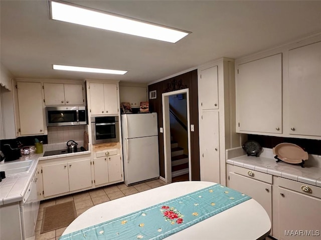 kitchen featuring stainless steel appliances, light tile patterned floors, backsplash, tile countertops, and white cabinetry