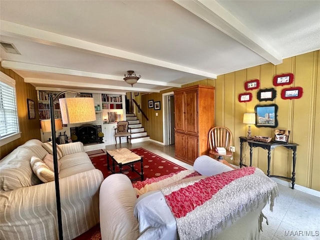 living room featuring baseboards, stairway, beam ceiling, visible vents, and wooden walls