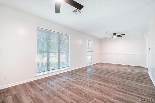 unfurnished room with wood finished floors, visible vents, a ceiling fan, and baseboards
