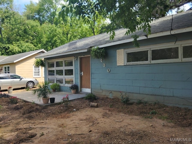 single story home featuring a patio, concrete block siding, and roof with shingles