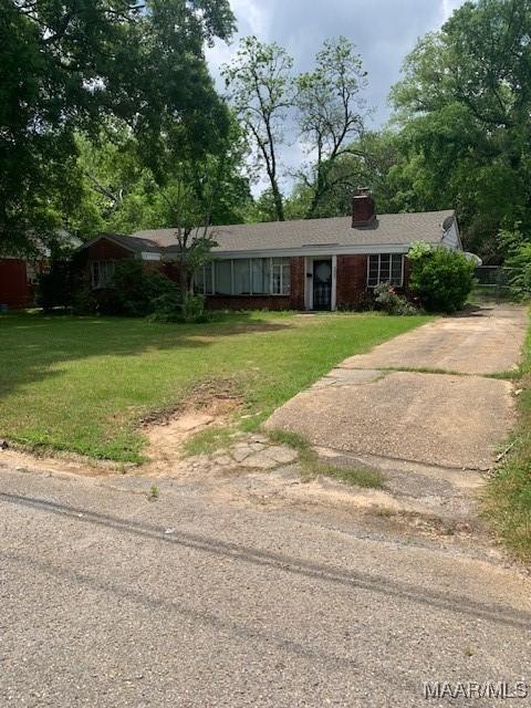 ranch-style house with a chimney, brick siding, and a front lawn