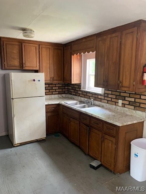 kitchen with brown cabinetry, a sink, light countertops, and freestanding refrigerator