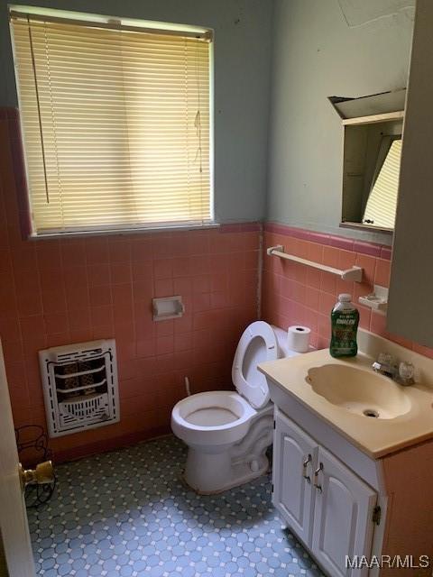 half bath with heating unit, toilet, wainscoting, and tile walls