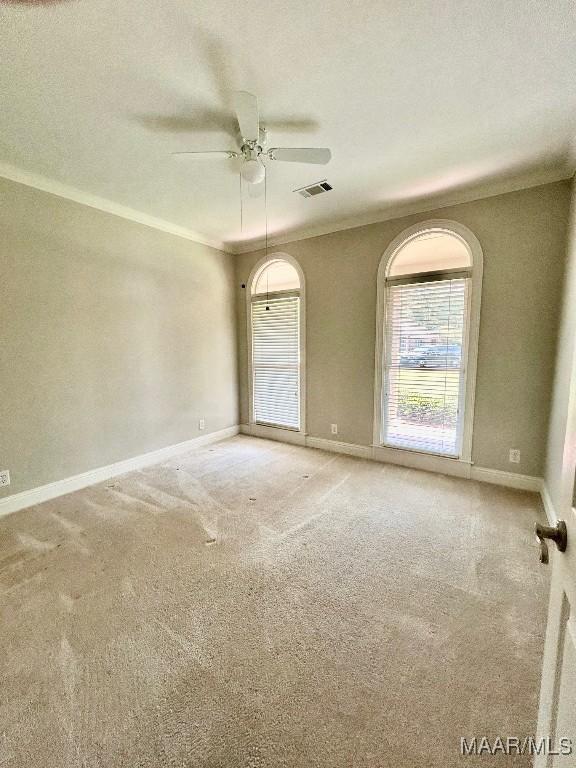 spare room with visible vents, ceiling fan, baseboards, ornamental molding, and carpet