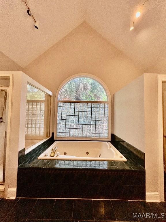 full bathroom with a tub with jets, rail lighting, and vaulted ceiling