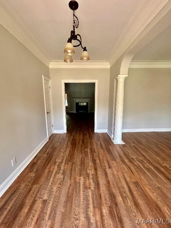 unfurnished dining area with ornamental molding, dark wood-style floors, arched walkways, and baseboards