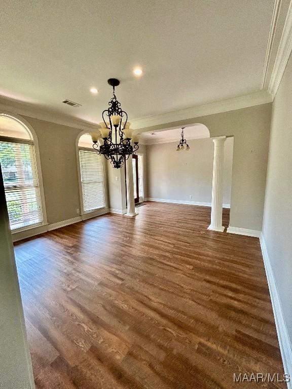 unfurnished dining area with wood finished floors, a chandelier, ornamental molding, and arched walkways