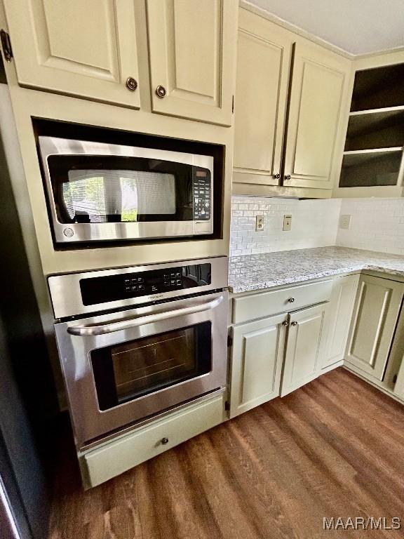 kitchen with light stone counters, stainless steel appliances, open shelves, backsplash, and dark wood-style flooring