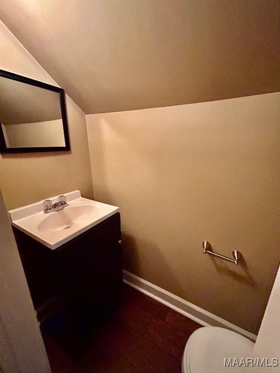 half bath with toilet, vanity, lofted ceiling, and baseboards