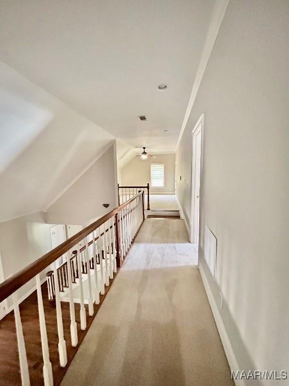 hallway featuring visible vents, baseboards, ornamental molding, vaulted ceiling, and carpet