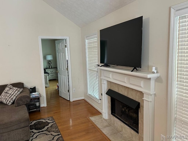 living room with a textured ceiling, baseboards, a tile fireplace, light wood-type flooring, and vaulted ceiling