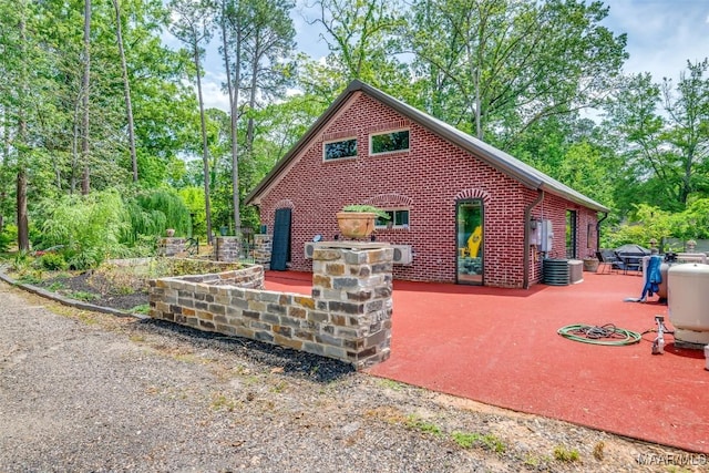 exterior space with central AC unit, a patio area, and brick siding