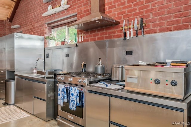kitchen featuring brick wall, stainless steel appliances, wall chimney range hood, vaulted ceiling, and a sink
