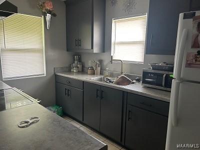 kitchen featuring stainless steel microwave, a sink, light tile patterned flooring, light countertops, and freestanding refrigerator