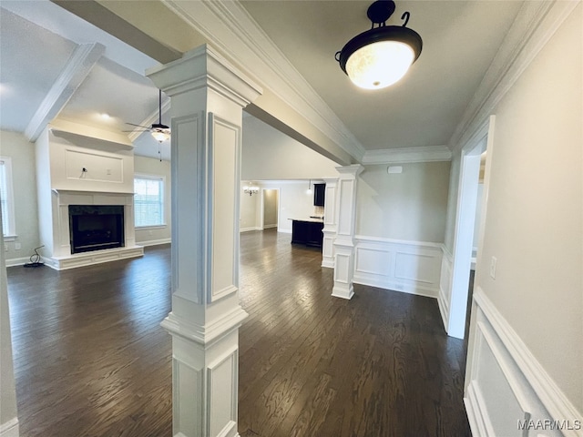 unfurnished living room with dark wood-type flooring, crown molding, a ceiling fan, ornate columns, and wainscoting