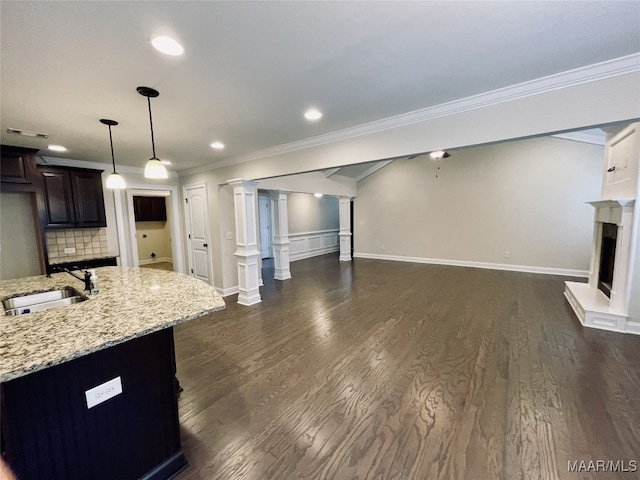 unfurnished living room featuring dark wood-style floors, a sink, a fireplace with raised hearth, crown molding, and visible vents