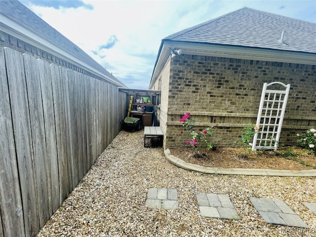 view of property exterior featuring brick siding, fence, and a shingled roof