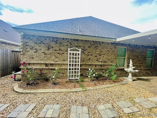 view of property exterior featuring fence, roof with shingles, and brick siding