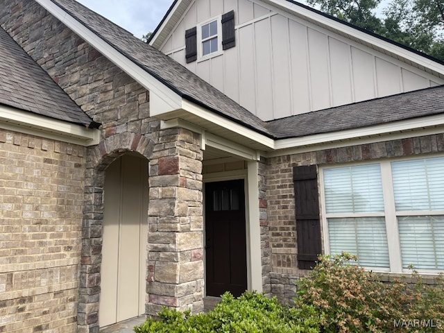 view of exterior entry with brick siding, board and batten siding, and roof with shingles