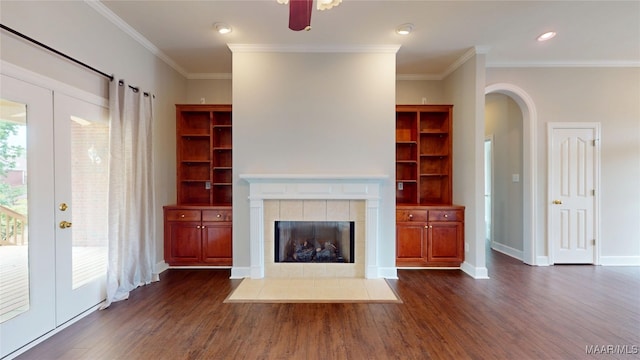 unfurnished living room featuring arched walkways, ornamental molding, dark wood-style floors, and a tiled fireplace