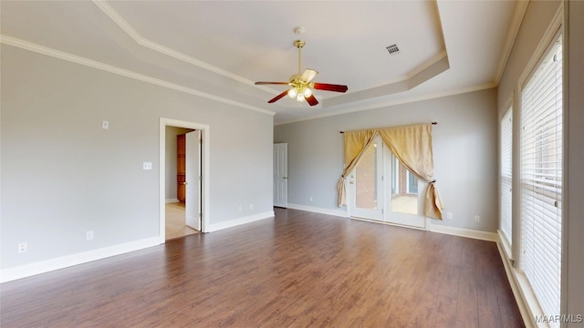 unfurnished room with visible vents, wood finished floors, baseboards, a tray ceiling, and a ceiling fan