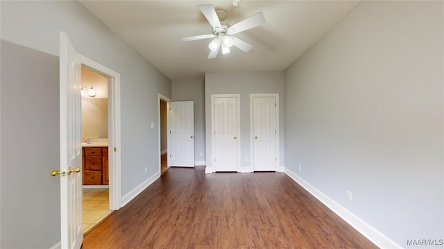 unfurnished bedroom featuring baseboards, a ceiling fan, multiple closets, and wood finished floors