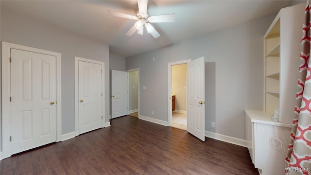 unfurnished bedroom with ceiling fan, baseboards, multiple closets, and wood finished floors