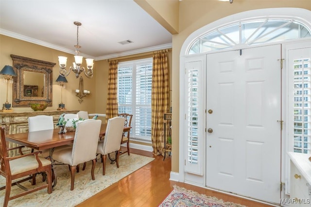 entrance foyer featuring visible vents, ornamental molding, wood finished floors, and a notable chandelier