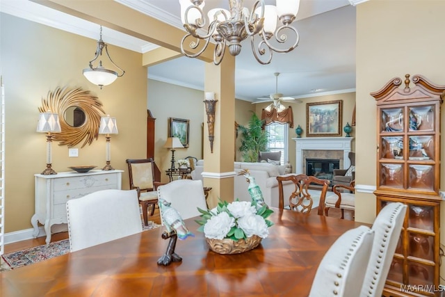 dining space with baseboards, a glass covered fireplace, ornamental molding, and ceiling fan with notable chandelier